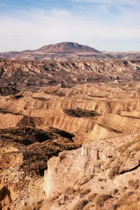 Granada Prints: Eroded cliffs and winding ravines in a desert landscape with mountains in the distance in Granada