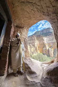 Adults Prints: Ethiopian Orthodox priest holding the hand cross at entrance of Abuna Yemata Guh church