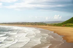 United Prints: Evening light casts long shadows on Rhossili Bay Beach with gentle waves and sandy shores in Swansea