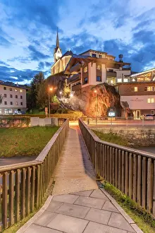 Walkway Prints: Evening view of church and buildings in Kaprun during summer with bridge and sky filled with clouds in Austria