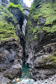 Flowing Prints: Exploring the deep canyon in Switzerland with a clear stream flowing below and a stone bridge above in daylight