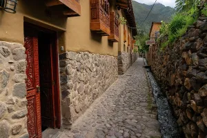 Balconies Prints: Exploring a narrow cobblestone street with stone buildings and a small water channel in a town in Peru during daytime