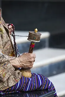 Bhutan Prints: A faithful Buddhist uses the traditional portable roller-book (prayer wheel), Bhutan