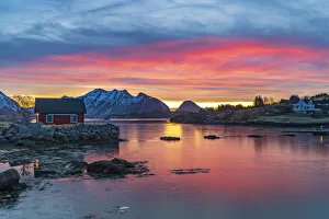 Lofoten Islands Prints: Fiery sky at sunrise over a red Rorbu facing the frozen sea
