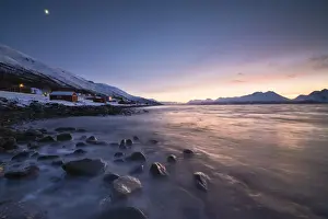 Winter Scene Prints: Fiery sky at sunset on typical Rorbu framed by snowy peaks and frozen sea, Djupvik