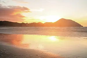 Zealand Prints: Fiery sunset reflects on wet sands at Wharariki Beach in New Zealand with mountains in the background