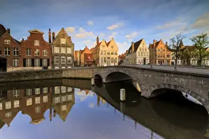 Bruges Prints: First light of sunrise on the historic buildings and bridge reflected in the typical canal