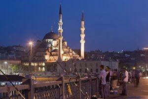 Fishermen on Galata Bridge, New Mosque illuminated in the evening, Istanbul