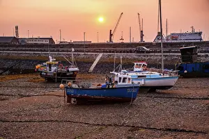 Silhouettes Prints: Fishing boats sit on the seabed at low tide during a hazy sunrise in St Peter Port harbor in Guernsey Channel Islands