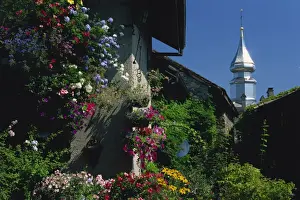 Yvoire Prints: Flower filled garden of village house with sparkling church spire beyond