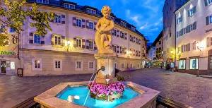 Salzburg Prints: Fountain in Stadtplatz during dusk with a sculpture, flowers, and buildings in Zell am See