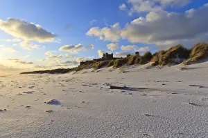Ripples Prints: Fresh Spring snow at dawn highlight ripples and marks in the sand beneath Bamburgh Castle
