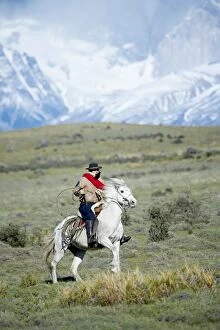 A gaucho riding his horse with Cuernos del Paine (Horns of Paine) mountains in the background