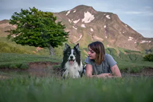 A girl and her border collie dog lying in the grass with a tree and mountain in the background, Emilia Romagna, Italy A girl and her border collie dog lying in the grass with a tree and mountain in the background, Emilia Romagna, Italy