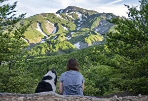 A girl sitting beside her border collie dog staring at a mountain landscape of Cusna Mountain, Emilia Romagna, Italy A girl sitting beside her border collie dog staring at a mountain landscape of Cusna Mountain, Emilia Romagna, Italy