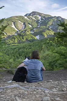 A girl sitting beside and hugging her border collie dog staring at a mountain landscape of Cusna Mountain A girl sitting beside and hugging her border collie dog staring at a mountain landscape of Cusna Mountain