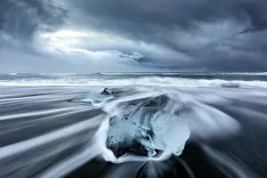 Glacier Prints: Glacier ice on black sand beach with waves washing up the beach on a stormy winter day