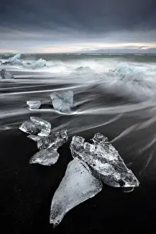Glassy pieces of ice on volcanic black sand beach with blurred waves, near Jokulsarlon Lagoon