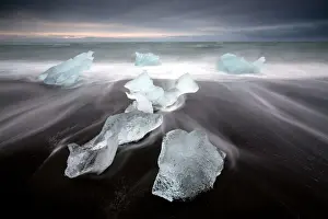 Black Sand Prints: Glassy pieces of ice on volcanic black sand beach with blurred waves