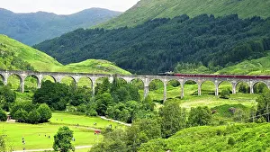 Charming Prints: Glenfinnan Viaduct shows steam train passing over arches against mountains in summer in Scotland