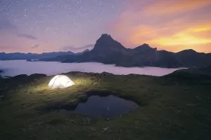 Nighttime Prints: A glowing tent sits on a grassy hill under a starlit sky