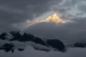 Range Prints: Golden light shines on Kawagebo Peak at dawn in Yunnan China with clouds surrounding the mountain