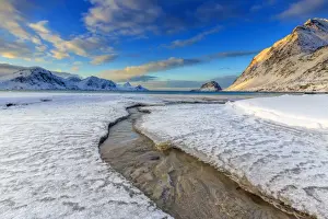 The golden sunrise reflected in a clear stream of the sea where the snow has melted