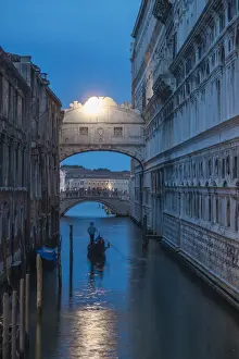 Gondolas pass under the Bridge of Sighs beside the Doges Palace in Venice at twilight