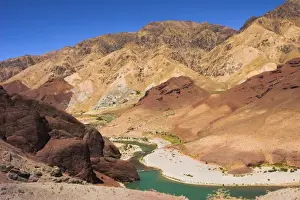 Hari Rud river flows through fertile valley at base of red rock mountains