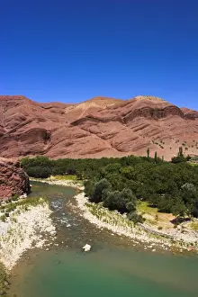 Hari Rud river flows through fertile valley at base of red rock mountains