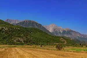 Albania Prints: Harvested fields at the base of hills with mountains in the background under a clear sky in southern Albania