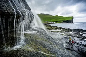 Pure Prints: High angle view of two hikers admiring a majestic waterfall standing on cliffs