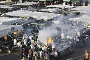 Cooking Prints: High view of food stalls, cooking and people in Djemma el Fna square in early evening in the Medina
