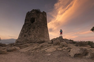 Cagliari Prints: Hiker admires sunset from the stone tower overlooking the bay, Porto Giunco, Villasimius