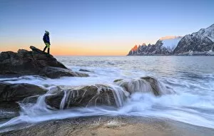 Contemplating Gallery: Hiker admires the waves of the icy sea crashing on the rocky cliffs at dawn, Tungeneset