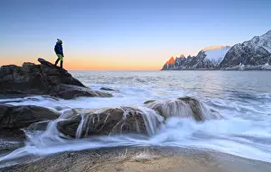 Alpenglow Prints: Hiker admires the waves of the icy sea crashing on the rocky cliffs at dawn, Tungeneset