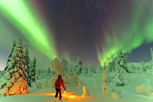 Recreational Pursuits Prints: Hiker with lantern standing in the snow in the frozen wood admiring Northern Lights (Aurora Borealis)