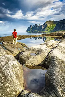 Hiker man contemplating the sharp rocks of mountain peaks standing beside rock pools