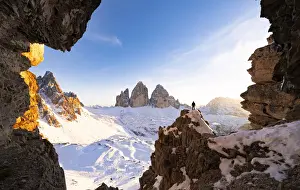 Mid Adult Man Prints: Hiker on rocks admiring Tre Cime di Lavaredo and Monte Paterno covered with snow
