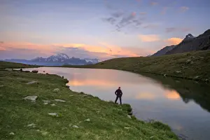 Lombardy Prints: Hiker on the shore admires the pink colors of dawn reflected in Lake Campagneda