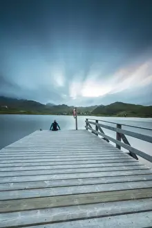 Thoughtful Prints: Hiker on wooden deck admires the sea illuminated by blue lights at night, Holdalsvatnet