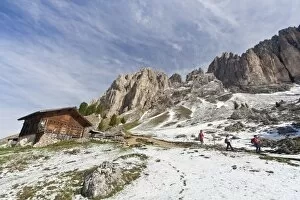 Hikers walking along the trail at the foot of the Sassolungo and Sassopiatto after a snowfall during springtime