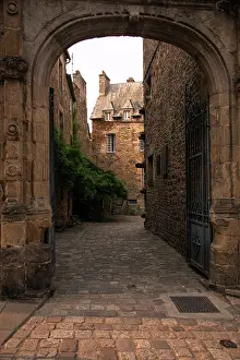 Cobbled Prints: Historic stone archway leads to cobbled street with medieval houses in Dinan