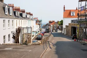 Parked Prints: Historic stone buildings line a narrow street with sea views in St Peter Port, Guernsey