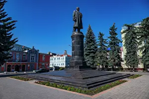 Center Prints: Historical statue of Lenin stands in Vladikavkaz surrounded by buildings and trees in a sunny day