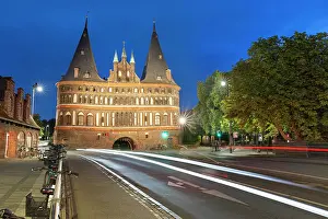 Vehicles Prints: Holsten Tower stands illuminated at night while vehicles pass in Lubeck