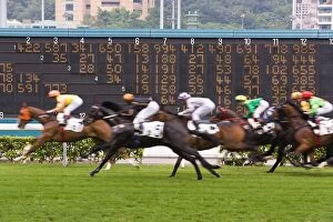 Horses race past large scoreboard during race at Happy Valley racecourse