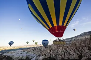 Hot air balloons flying among rock formations at sunrise in the Red Valley, Goreme National Park