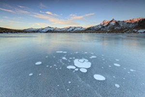 Blue Ice Prints: Ice bubbles on the frozen surface of Andossi Lake at sunrise, Spluga Valley, Valtellina