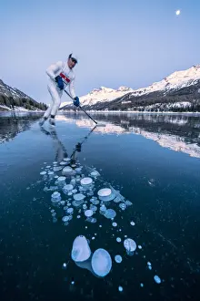 Engadine Prints: Ice hockey player man skating on Lake Sils covered in ice bubbles at dusk, Engadine